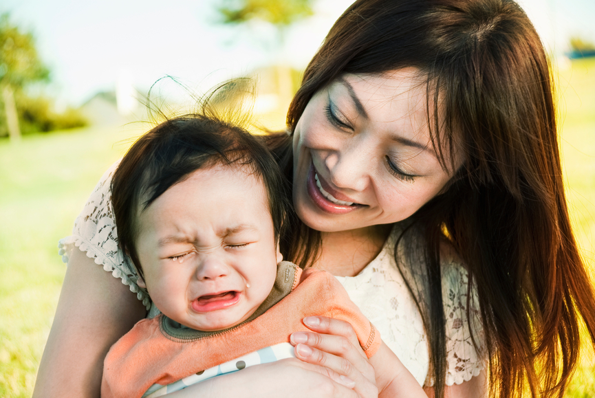 A Japanese mother holding her crying 6-month old mixed-race boy (Japanese-Filipino-Caucasian) with love at a park.
